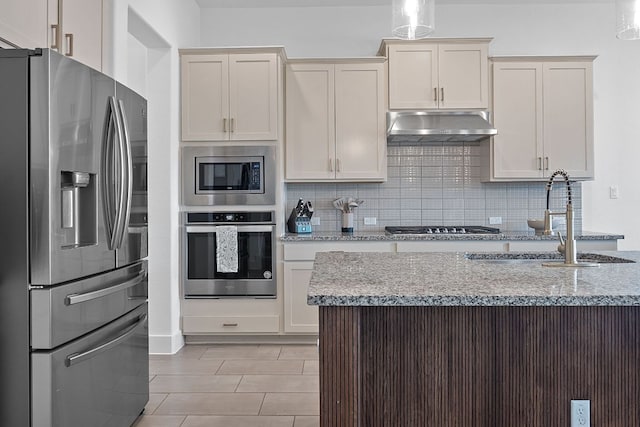 104 Meadow Wood Cv, Georgetown, TX 78626 - kitchen featuring appliances with stainless steel finishes, under cabinet range hood, a sink, decorative backsplash, and light stone counters