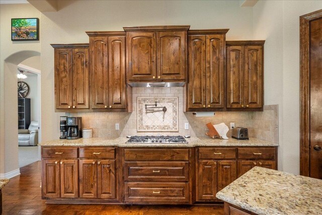 102 Standing Oak Dr, Georgetown, TX 78633 - kitchen with stainless steel gas stovetop, tasteful backsplash, light stone countertops, dark wood-style flooring, and arched walkways