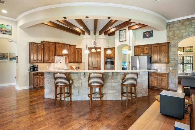 102 Standing Oak Dr, Georgetown, TX 78633 - kitchen with arched walkways, appliances with stainless steel finishes, a breakfast bar, dark wood finished floors, and backsplash