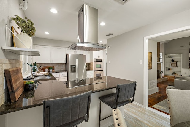 13007 Stillforest St, Austin, TX 78729 - kitchen with stainless steel appliances, island exhaust hood, a sink, a peninsula, and light wood-style floors