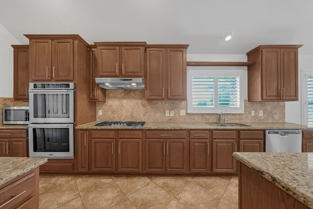 20700 Windmill Ridge St, Pflugerville, TX 78660 - kitchen featuring appliances with stainless steel finishes, under cabinet range hood, tasteful backsplash, and brown cabinetry