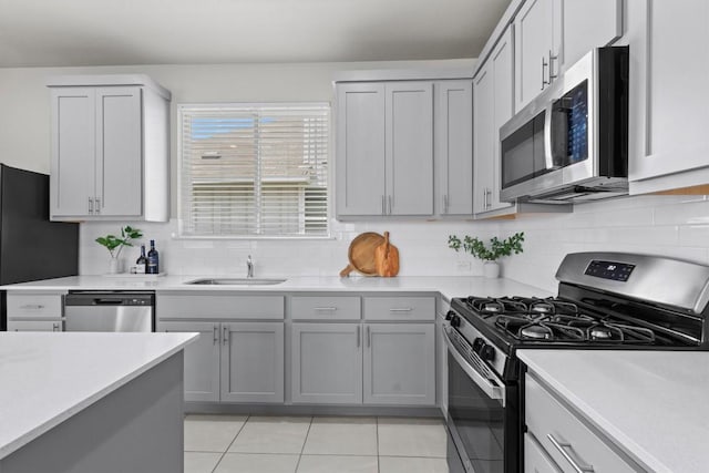 299 Fabion St, Kyle, TX 78640 - kitchen with appliances with stainless steel finishes, light tile patterned floors, light countertops, gray cabinets, and decorative backsplash