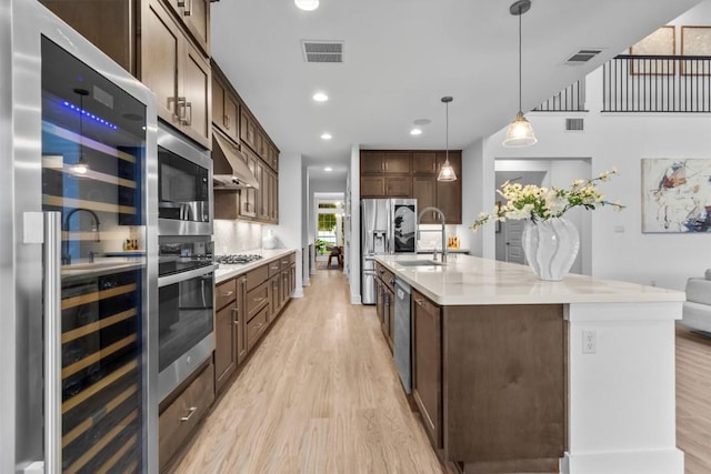1329 Da Vinci Trl, Leander, TX 78641 - kitchen with beverage cooler, stainless steel appliances, light wood finished floors, dark brown cabinets, and recessed lighting