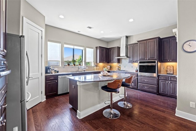1017 Sue Ann Rose Dr, Austin, TX 78717 - kitchen featuring appliances with stainless steel finishes, wall chimney range hood, a kitchen island, tasteful backsplash, and a kitchen bar