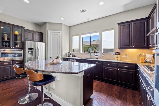 1017 Sue Ann Rose Dr, Austin, TX 78717 - kitchen featuring a kitchen island, stainless steel appliances, light stone countertops, dark wood-type flooring, and a kitchen breakfast bar