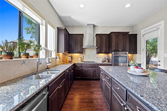 1017 Sue Ann Rose Dr, Austin, TX 78717 - kitchen with wall chimney range hood, stainless steel appliances, a sink, dark wood-style flooring, and light stone counters