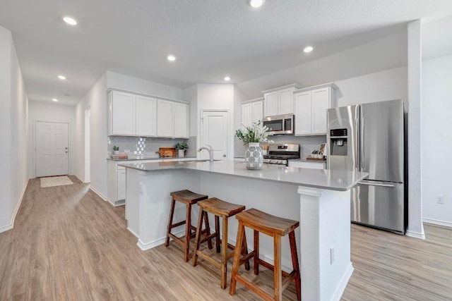 3109 Windy Vane Dr, Pflugerville, TX 78660 - kitchen with appliances with stainless steel finishes, light wood finished floors, a kitchen island with sink, white cabinetry, and a kitchen breakfast bar