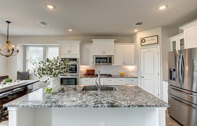 20517 Kangal Ct, Pflugerville, TX 78660 - kitchen with stainless steel appliances, a sink, a chandelier, white cabinets, and a kitchen island with sink