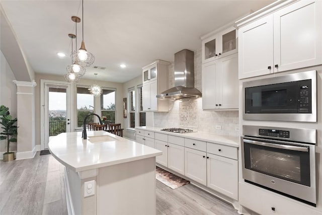 5400 Alonso Dr, Austin, TX 78738 - kitchen featuring stainless steel appliances, wall chimney range hood, a sink, light wood finished floors, and tasteful backsplash