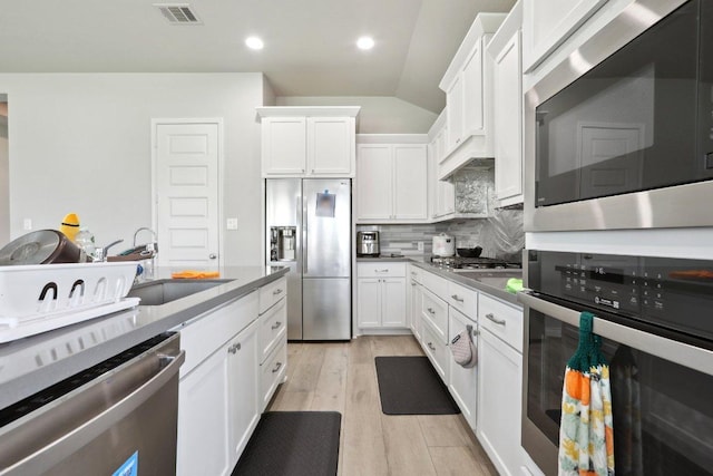 13212 Carol Lawler Ln, Manor, TX 78653 - kitchen featuring appliances with stainless steel finishes, backsplash, light wood-style floors, white cabinetry, and lofted ceiling