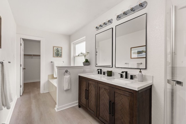 8005 Willet Trl, Austin, TX 78745 - bathroom featuring double vanity, wood finished floors, a garden tub, baseboards, and a spacious closet
