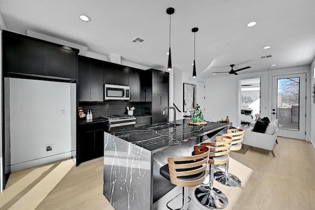 1117 Lawson Ln Unit 2, Austin, TX 78702 - kitchen with dark cabinetry, stainless steel appliances, a sink, light wood-style floors, and recessed lighting