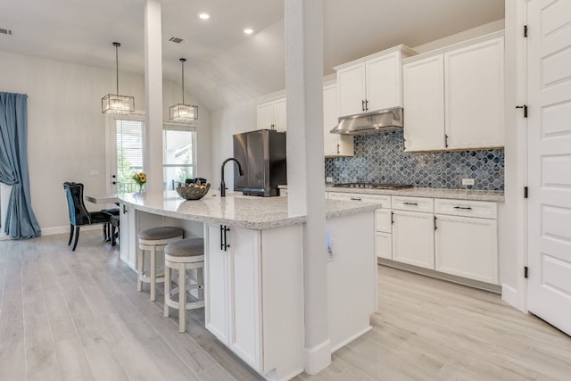603 Arundel Rd, Austin, TX 78738 - kitchen featuring appliances with stainless steel finishes, under cabinet range hood, decorative backsplash, vaulted ceiling, and a center island with sink