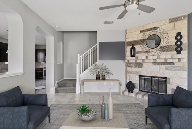144 Holstein St, Hutto, TX 78634 - tiled living room featuring arched walkways, stairs, a ceiling fan, and a stone fireplace