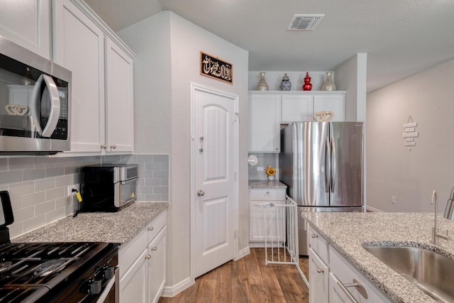 19413 Abigail Fillmore Rd, Manor, TX 78653 - kitchen featuring stainless steel appliances, a sink, white cabinetry, light wood-style floors, and tasteful backsplash