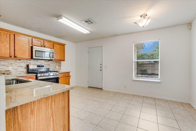 8520 Chick Pea Ln, Austin, TX 78748 - kitchen featuring stainless steel appliances, decorative backsplash, light stone counters, light tile patterned flooring, and brown cabinets