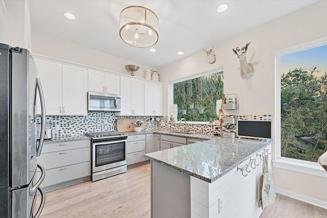 19506 Inverness Dr, Lakeway, TX 78669 - kitchen featuring appliances with stainless steel finishes, light wood-type flooring, light stone countertops, backsplash, and a peninsula