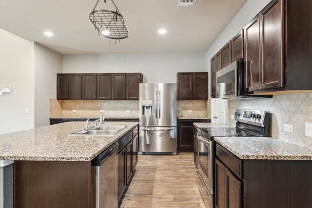 1008 Comal Run, Hutto, TX 78634 - kitchen with appliances with stainless steel finishes, light wood-style floors, a sink, dark brown cabinetry, and recessed lighting