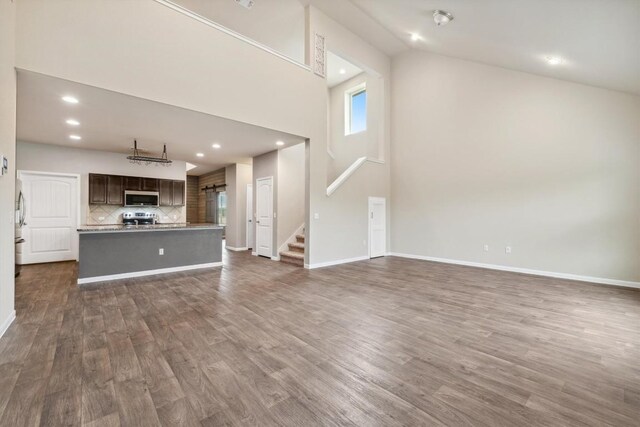 1008 Comal Run, Hutto, TX 78634 - unfurnished living room with dark wood-style flooring, high vaulted ceiling, recessed lighting, stairs, and baseboards