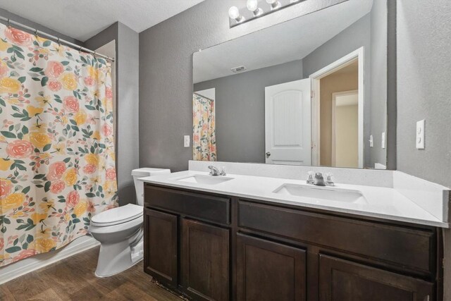 1008 Comal Run, Hutto, TX 78634 - bathroom with a textured wall, wood finished floors, double vanity, toilet, and a shower with curtain