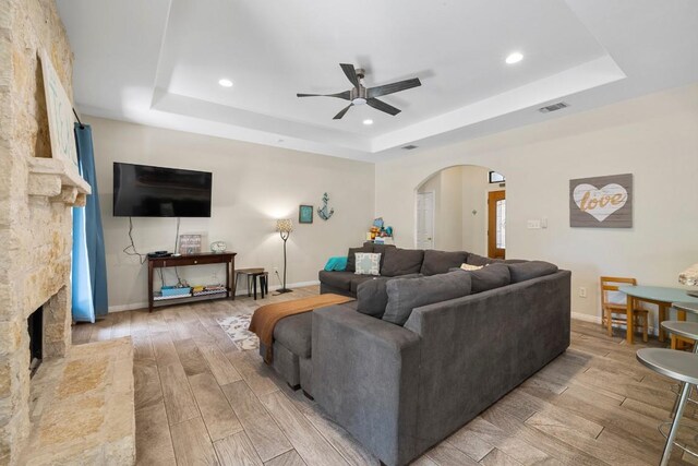 15100 General Williamson Dr, Austin, TX 78734 - living room with a tray ceiling, ceiling fan, arched walkways, a stone fireplace, and light wood finished floors