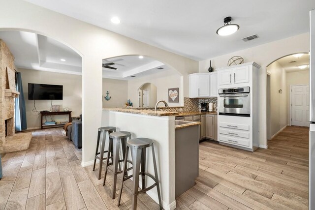 15100 General Williamson Dr, Austin, TX 78734 - kitchen with stainless steel oven, a tray ceiling, light wood-type flooring, a breakfast bar, and a peninsula