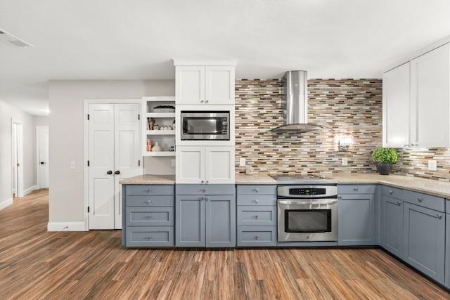 101 Explorer Cv, Lakeway, TX 78734 - kitchen featuring wall chimney exhaust hood, appliances with stainless steel finishes, wood finished floors, backsplash, and white cabinets