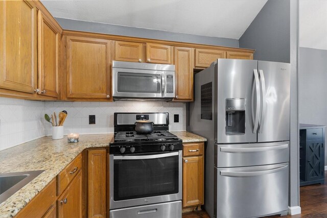 2000 Holly Springs Dr, Taylor, TX 76574 - kitchen featuring stainless steel appliances, decorative backsplash, light stone counters, brown cabinetry, and lofted ceiling