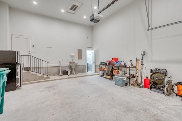 garage with a garage door opener, recessed lighting, freestanding refrigerator, and electric panel