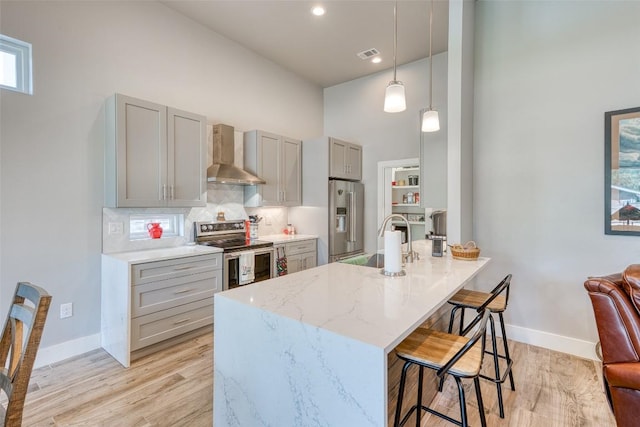kitchen featuring appliances with stainless steel finishes, wall chimney exhaust hood, a sink, gray cabinets, and a breakfast bar