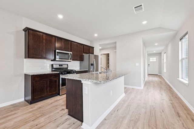 136 Ellinger Rd, Georgetown, TX 78626 - kitchen with stainless steel appliances, light wood-type flooring, a center island with sink, dark brown cabinetry, and light stone counters