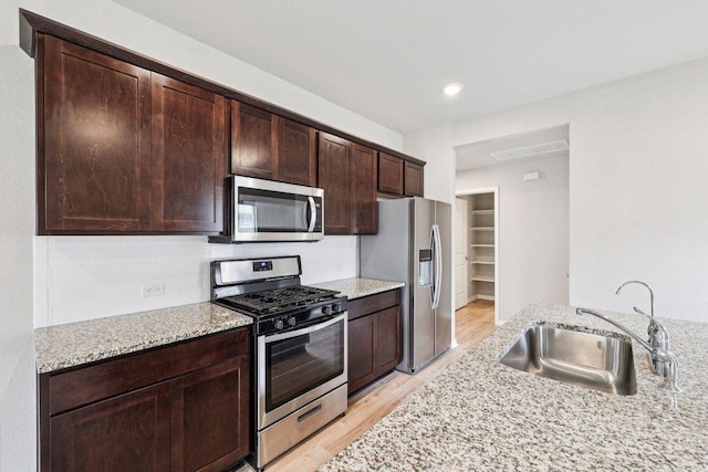 136 Ellinger Rd, Georgetown, TX 78626 - kitchen with appliances with stainless steel finishes, a sink, light wood finished floors, light stone countertops, and dark brown cabinets