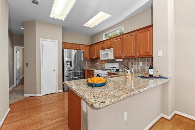 206 Whispering Wind Dr, Georgetown, TX 78633 - kitchen with white appliances, a peninsula, light stone counters, and light wood finished floors