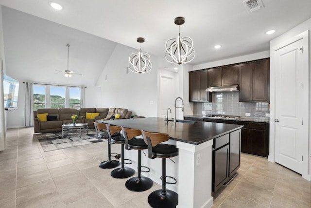 8119 Purple Aster Pass, Leander, TX 78645 - kitchen featuring dark countertops, under cabinet range hood, backsplash, dark brown cabinets, and a kitchen bar