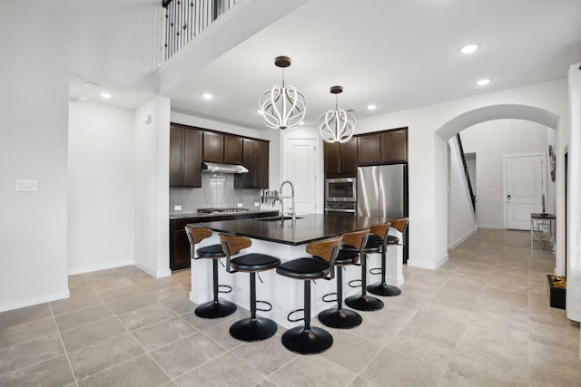 8119 Purple Aster Pass, Leander, TX 78645 - kitchen with arched walkways, stainless steel appliances, under cabinet range hood, dark brown cabinets, and a breakfast bar area