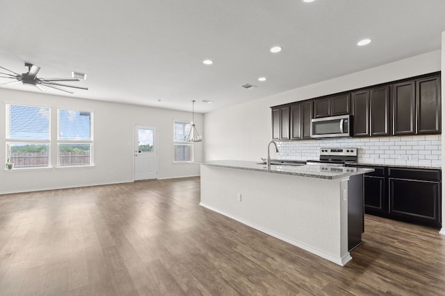 709 Hummingbird Ln, Leander, TX 78641 - kitchen featuring stainless steel appliances, dark wood-type flooring, a center island with sink, backsplash, and recessed lighting