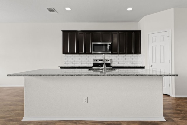 709 Hummingbird Ln, Leander, TX 78641 - kitchen featuring appliances with stainless steel finishes, a kitchen island with sink, stone counters, decorative backsplash, and baseboards