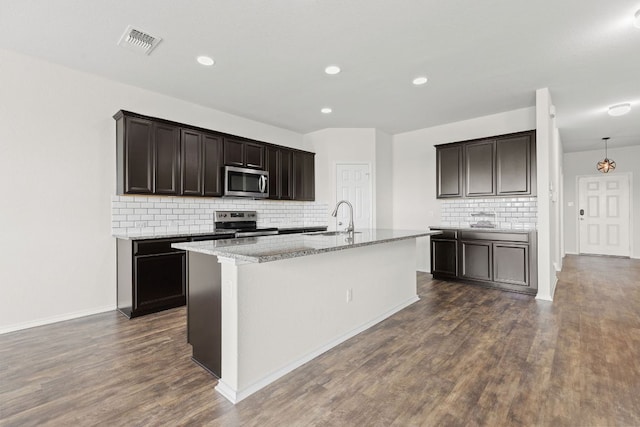 709 Hummingbird Ln, Leander, TX 78641 - kitchen with stainless steel appliances, tasteful backsplash, a sink, dark wood-style flooring, and a center island with sink