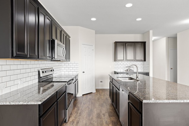 709 Hummingbird Ln, Leander, TX 78641 - kitchen featuring appliances with stainless steel finishes, a sink, dark wood finished floors, light stone counters, and a kitchen island with sink