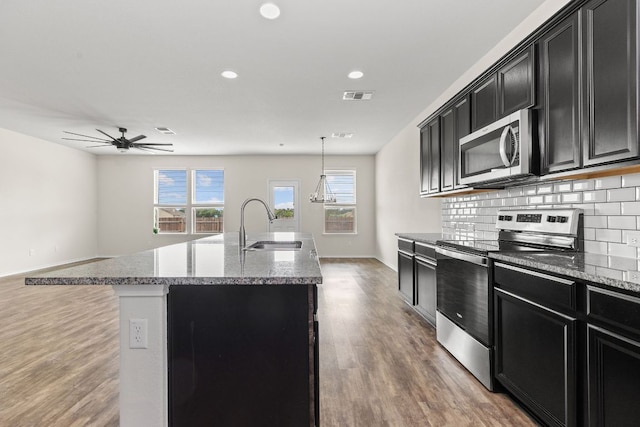 709 Hummingbird Ln, Leander, TX 78641 - kitchen with appliances with stainless steel finishes, dark cabinets, wood finished floors, an island with sink, and a ceiling fan