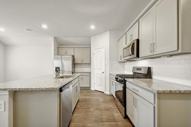 210 Briggs Ln, San Marcos, TX 78666 - kitchen with appliances with stainless steel finishes, wood finished floors, decorative backsplash, recessed lighting, and an island with sink