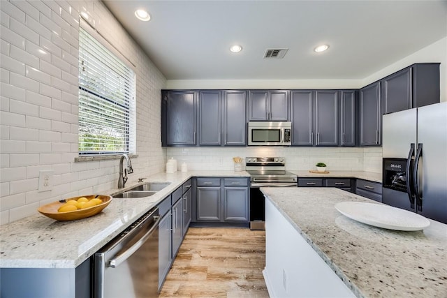 14605 Naruna Way, Pflugerville, TX 78660 - kitchen featuring appliances with stainless steel finishes, a sink, light wood-style flooring, light stone counters, and tasteful backsplash
