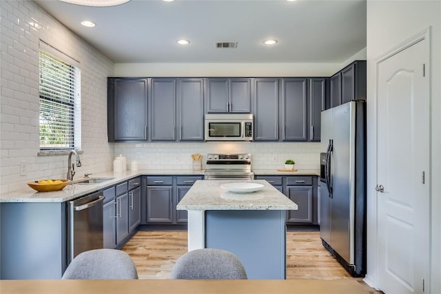 14605 Naruna Way, Pflugerville, TX 78660 - kitchen featuring stainless steel appliances, a sink, a center island, light wood-type flooring, and decorative backsplash