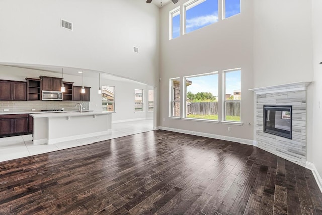 505 Fair Oaks Dr, Georgetown, TX 78628 - unfurnished living room with light wood finished floors, a towering ceiling, ceiling fan, a tiled fireplace, and a sink