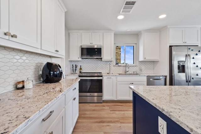 515 Circle Dr, Sunrise Beach, TX 78643 - kitchen with stainless steel appliances, a sink, light wood-style floors, white cabinets, and backsplash