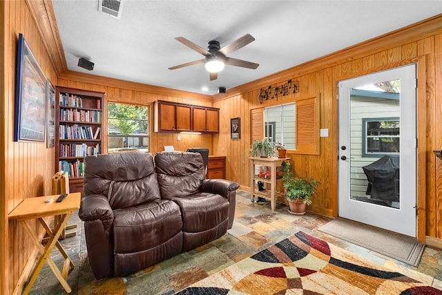 2301 Del Curto Rd, Austin, TX 78704 - living room featuring wood walls, stone tile floors, a ceiling fan, ornamental molding, and baseboards