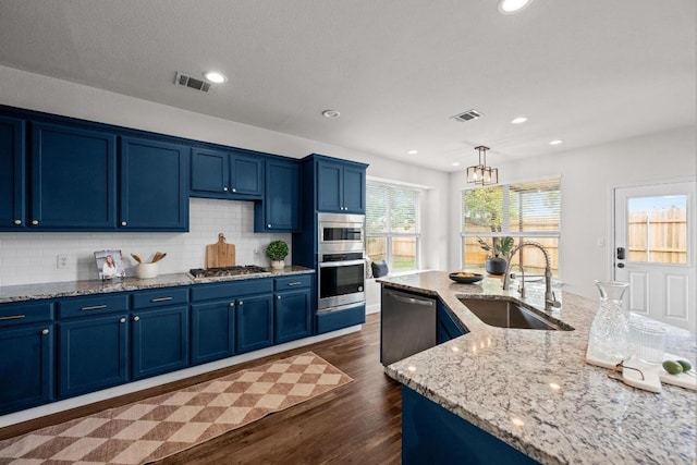 122 Retama Dr, Georgetown, TX 78626 - kitchen with stainless steel appliances, blue cabinetry, a sink, dark wood-style flooring, and tasteful backsplash