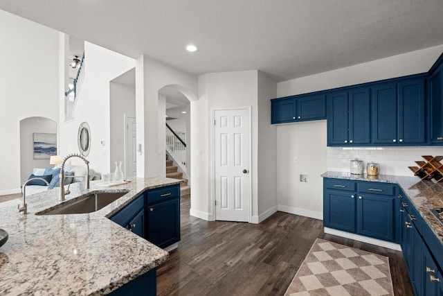 122 Retama Dr, Georgetown, TX 78626 - kitchen featuring a sink, blue cabinetry, light stone counters, arched walkways, and dark wood finished floors