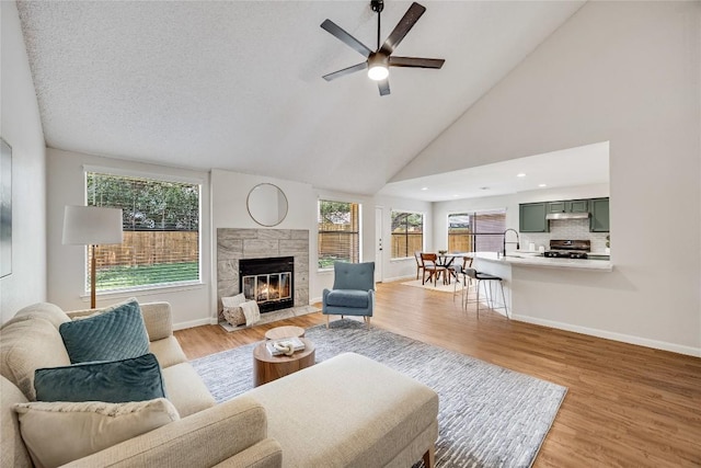 12910 Steeple Chase Dr, Austin, TX 78729 - living room featuring a ceiling fan, a tiled fireplace, healthy amount of natural light, light wood-type flooring, and high vaulted ceiling