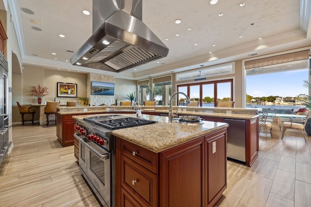 101 Matern Ct, Horseshoe Bay, TX 78657 - kitchen with a raised ceiling, wall chimney exhaust hood, stainless steel appliances, an island with sink, and crown molding